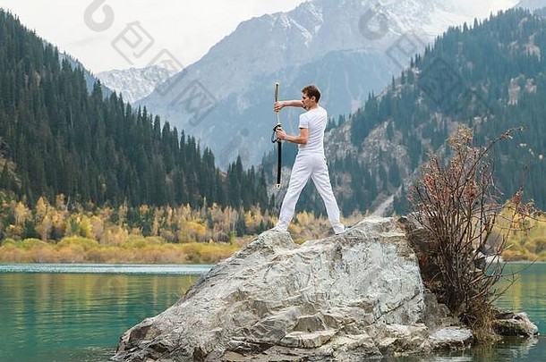 一个年轻人站在一块大石头上，手里拿着一把日本剑。