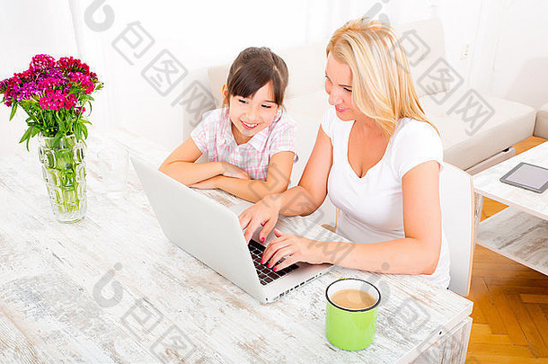 一位母亲带着女儿在家看笔记本电脑。