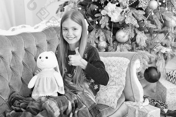 女孩拇指可爱的兔子圣诞节树小女孩持有兔子玩具孩子玩软玩具小孩子快乐微笑现在圣诞节玩具
