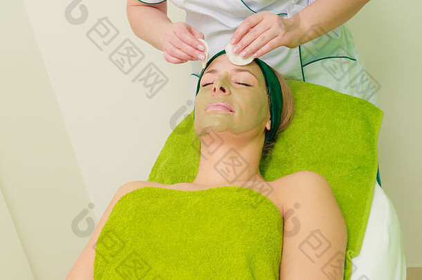 美容师在沙龙里擦去女人脸上的绿藻泥面膜。spa理念中的美容、放松、护肤、健康。