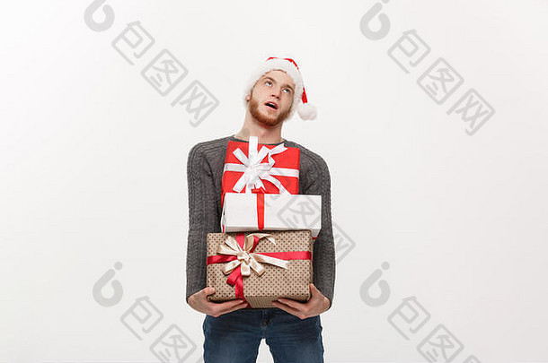 圣诞节概念年轻的英俊的男人。胡子持有重礼物疲惫面部表达式白色背景