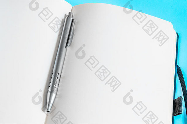 浅蓝背景下笔记本空白页上的金属圆珠笔