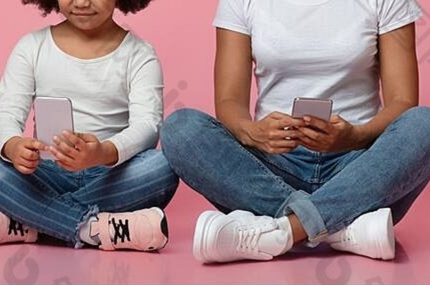 小玩意和儿童。带着智能手机的黑人小女孩和她的妈妈