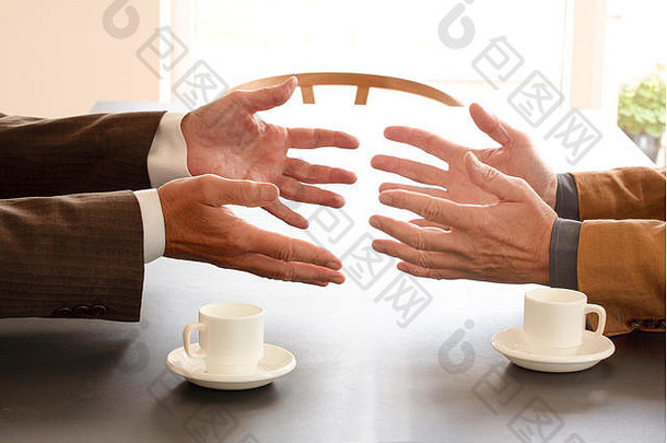 两位商人在桌子旁交谈时伸出的手。桌子上有两杯咖啡。商务谈判还是工作面试形象