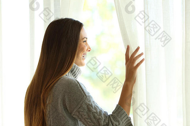 一个快乐的女人打开窗户的窗帘，在户外温暖的灯光下享受新的一天