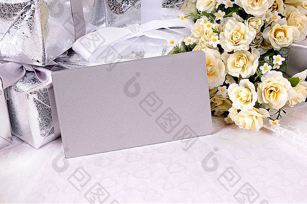 银灰色信封或请柬，带有几件结婚礼物和白色玫瑰花束，放在新娘花边上。的空间。