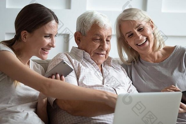 微笑的年长父母和成年女儿一起使用笔记本电脑