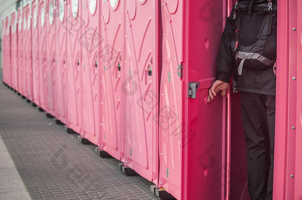 一个男人走进一排很长的粉红色便携式厕所。