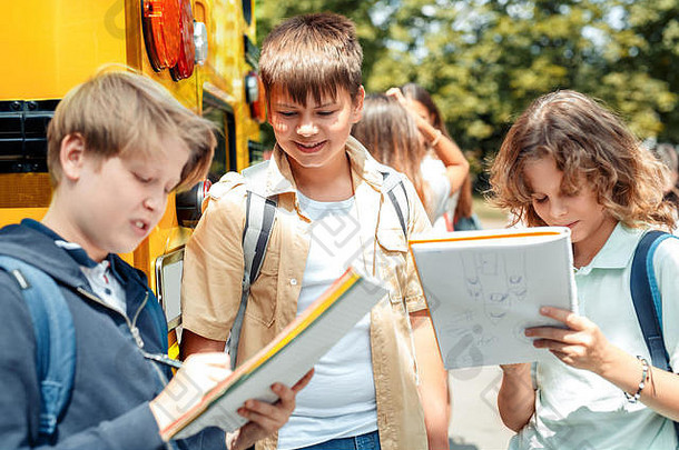 同学们坐公交车上学，男生们在笔记本上做作业，笑得很开心