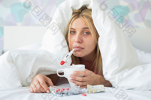 悲伤的女人的画像，拿着咖啡杯在床上取暖，被子裹着