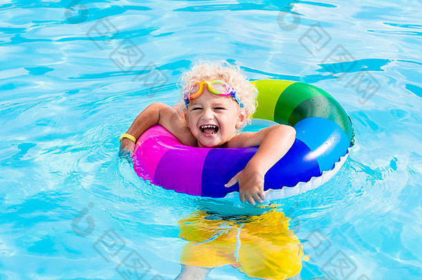 炎炎夏日，快乐的小男孩在室外游泳池里玩着五颜六色的充气戒指。孩子们学习游泳。儿童水玩具。儿童游戏