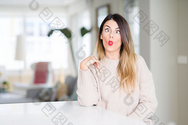 年轻漂亮的女人穿着冬天的毛衣在家里用嘴唇做鱼脸，疯狂而滑稽的手势。滑稽的表情。
