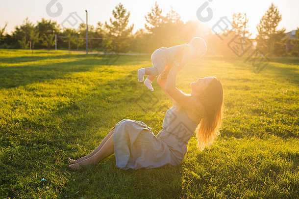 阳光明媚的日子里，年轻女子和男孩在草地上。夏日夕阳上的幸福家庭。妈妈带着孩子。