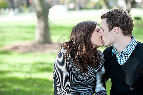 一对浪漫的情侣在公园里的阳光下接吻。