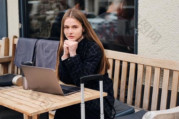美丽的休闲女孩专心地相机坐着户外咖啡馆移动PC手提箱