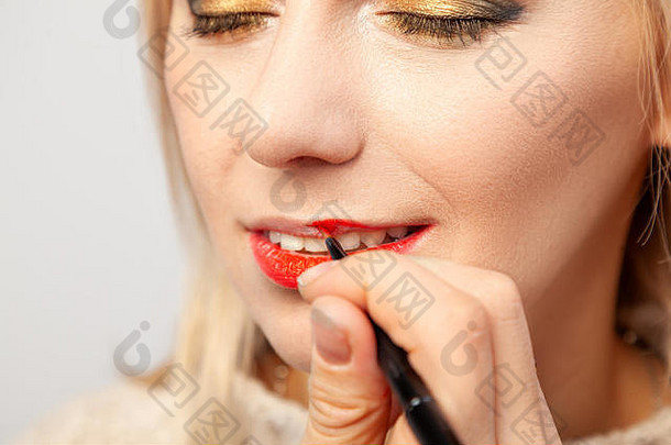 化妆师在工作室里用手上的刷子在模特的嘴唇上涂上一个红色唇膏的化妆品。