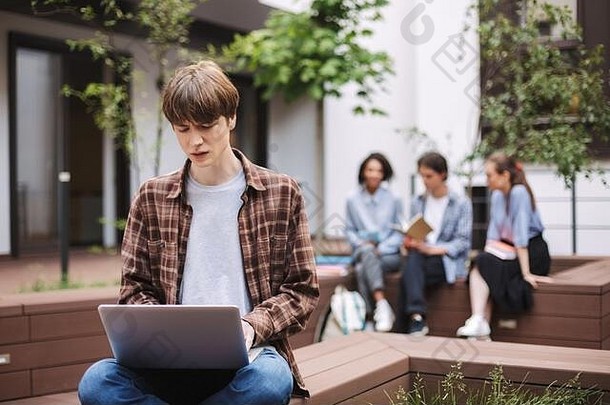 照片心烦意乱年轻的男人。坐着板凳上可悲的是工作移动PC支出时间院子里大学学生背景