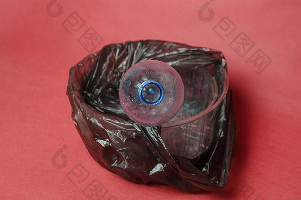 塑料透明空瓶，装在一个黑色袋子里，装在一个红色背景的容器里，并留有文本的空间。塑料对环境污染的概念
