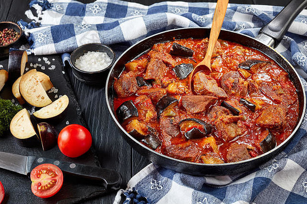 茄子炖牛肉-用平底锅在黑木桌上炖着Khoresht Bademjan，配上厨房毛巾和配料，波斯美食，俯瞰，clo