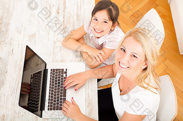 一位母亲带着女儿在家看笔记本电脑。