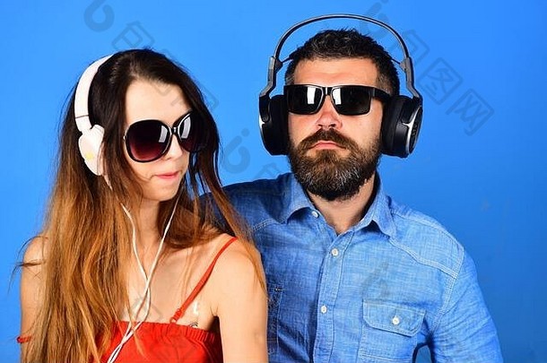 留着胡子的男人和<strong>女孩</strong>在蓝色背景下<strong>唱歌</strong>。相爱的情侣戴着耳机和太阳镜。面容严肃的音乐迷喜欢音乐，喜欢空间。派对和音乐概念。