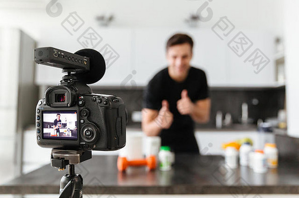 微笑年轻的男人。拍摄视频博客集健康的食物添加剂站厨房表格显示拇指手势