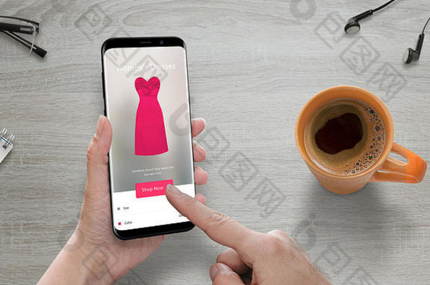 使用现代手机进行网上购物。女人在网上商店买粉红色的衣服。具有圆形边缘的现代智能手机。咖啡在旁边。