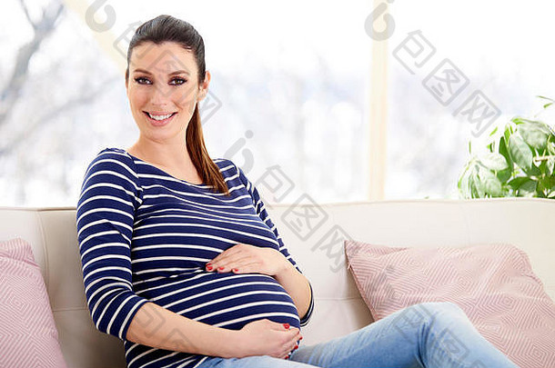 美丽的怀孕了女人手婴儿撞坐着沙发放松首页
