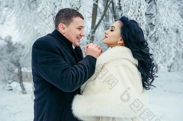 这对快乐美丽的新婚夫妇的敏感肖像。新郎正在冬天的森林里为他迷人的黑发新娘取暖。