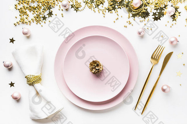 白色背景上的粉红色餐具、金色银器和派对装饰的圣诞餐桌。顶视图。圣诞晚餐。