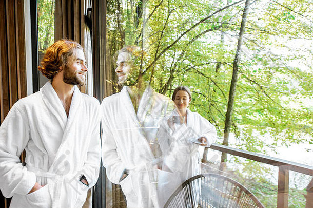 年轻的夫妇浴袍站窗口美丽的视图森林现代酒店房间