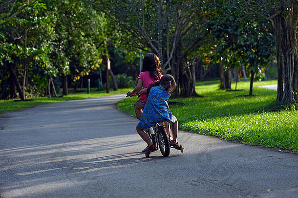 夏日阳光下，两个女孩坐在一辆自行车上在公园里骑自行车的<strong>可爱照片</strong>