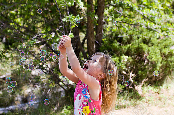一个小女孩在玩泡泡，并试图用棍子把泡泡戳破。
