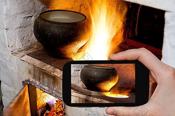 拍摄食物概念-游客拍摄俄罗斯火<strong>炉</strong>的火<strong>炉</strong>和智能手机上带有烤箱叉的旧铸铁锅