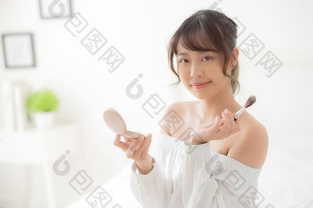 美女肖像：年轻的亚洲女人微笑着，在卧室里用刷子刷脸颊化妆，美丽的女孩拿着腮红
