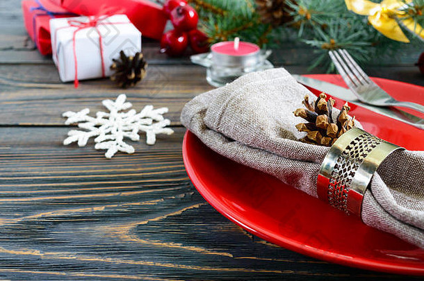 圣诞餐桌布置。黑色木质背景上圣诞树的红色盘子、叉子、刀、蜡烛、餐巾纸、礼品枝。空间。圣诞节X