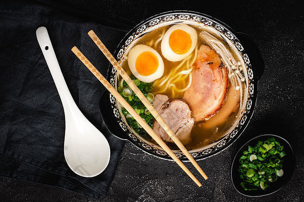 日本拉面汤，乌冬面，猪肉，鸡蛋和葱，深色石头背景