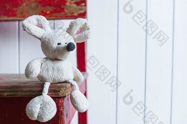 一只年老的小白鼠坐在白色墙壁背景下的一把旧红色椅子上。童年和老年孤独的概念。