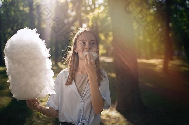 肖像漂亮的年轻的女孩吃棉花糖果公园