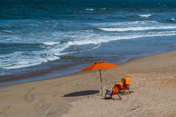 下午晚些时候，一把橙色雨伞和两把沙滩椅在北卡罗来纳州的Duck面向大海。
