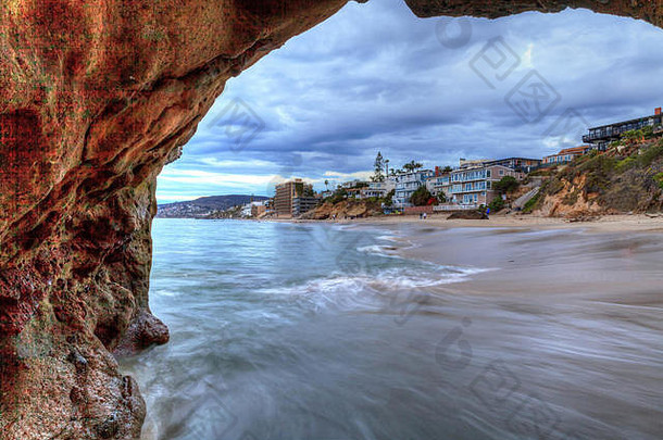 日落透过美国加利福尼亚州拉古纳海滩的岩石锁孔，击中珍珠街海滩沿岸的房屋