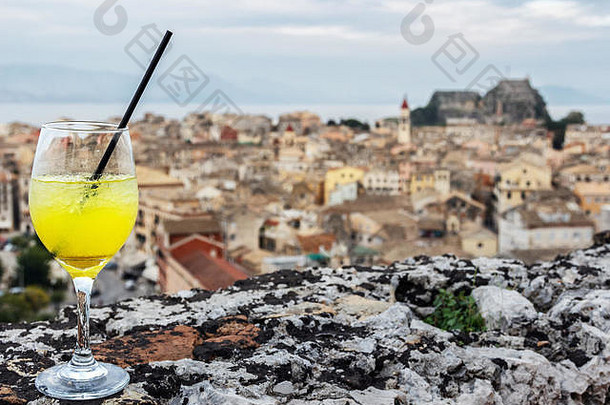 在一个户外屋顶酒吧里，一杯黄橙汁和一根吸管，鸟瞰希腊科尔夫岛上的科尔夫古城