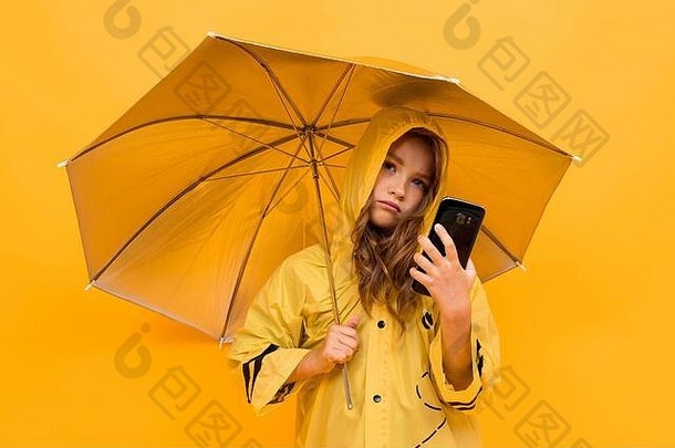 黄色背景上，一个穿着银色雨衣、手拿电话的开伞的旅行女孩的彩色照片