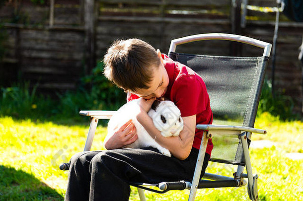 一个患有自闭症、阿斯伯格综合症和多动症的英俊快乐的小男孩在家里的花园里抱着他最喜欢的宠物兔子