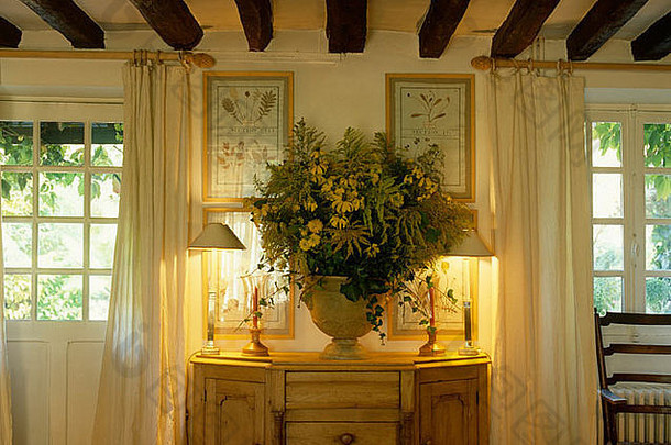 在有光束天花板的房间里，放在松木橱柜上的花瓶里点燃的灯和鲜花