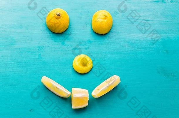 蓝色背景上一半成熟的黄色水果做成的笑脸俯视图、快乐饮食、柠檬和夏日概念。