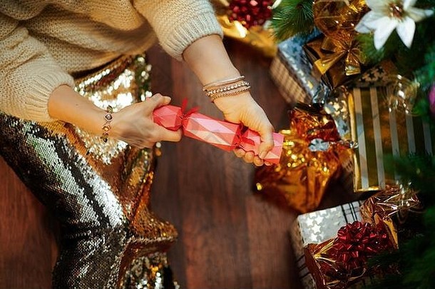 特写镜头：在装饰过的圣诞树下，一位穿着金色亮片裙子和白色毛衣的优雅女士在礼物盒旁撕扯着维多利亚时代的圣诞饼干。