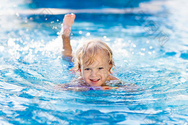 在热带度假胜地的室外游泳池里学习游泳的孩子。孩子们学习游泳。幼儿的锻炼和训练。穿着五颜六色衣服的小男孩