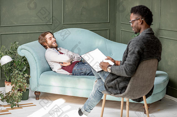 年轻的高加索人男人。参观非洲心理学家说谎舒适的沙发上心理会话绿色办公室