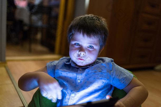 孩子年坐着房间看平板电脑脸突出显示蓝色的平板电脑屏幕